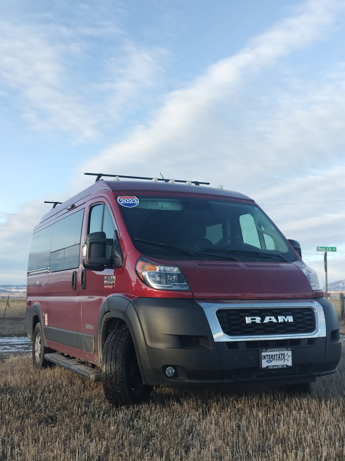 A red Pleasure-Way Tofino camper van, an RV rental, parked in a dry field under a cloudy sky, ready for a road trip.