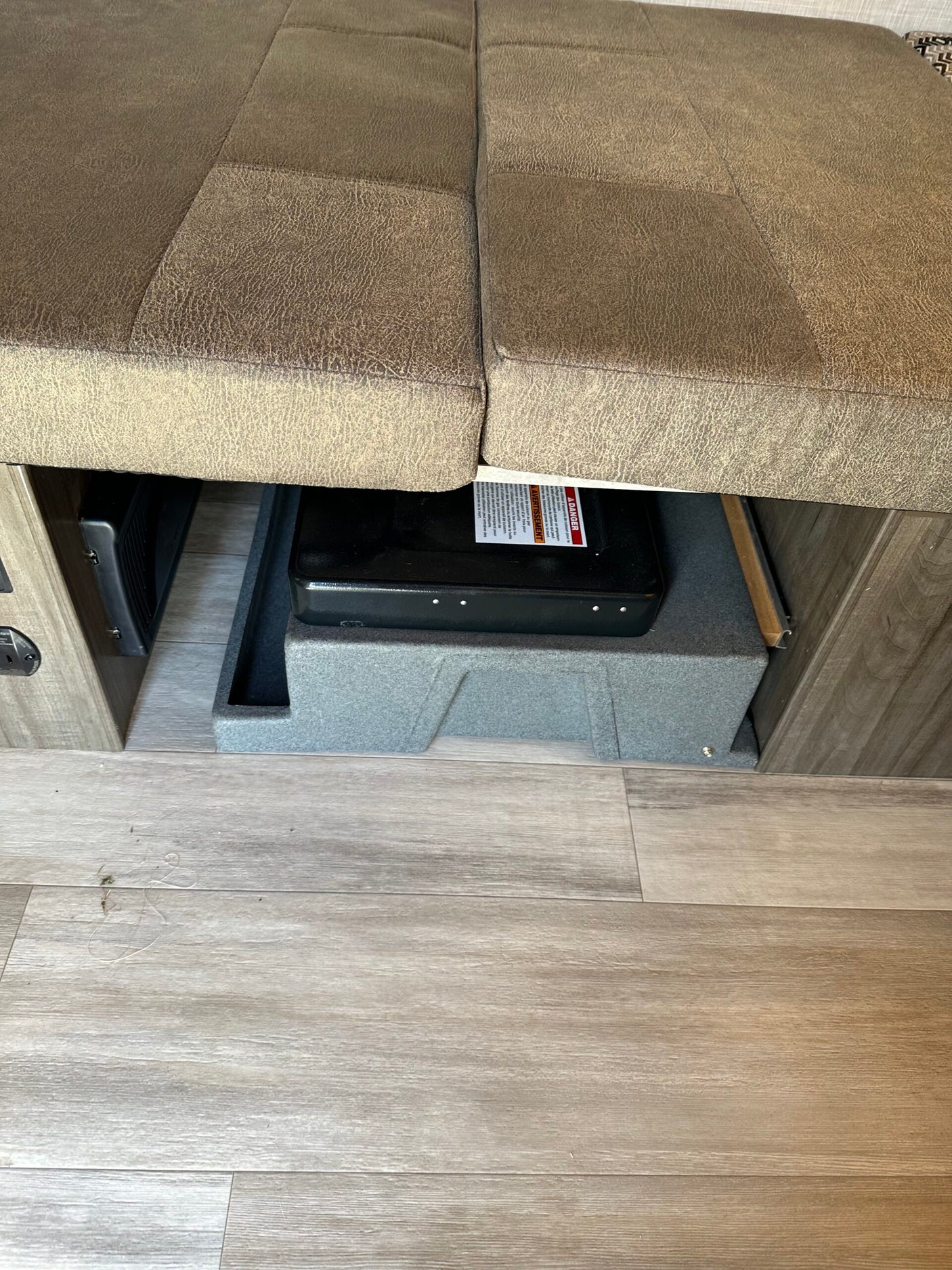 RV rental: Under-bench storage featuring a portable stove, an RV heating/cooling vent, and durable wood-look flooring.