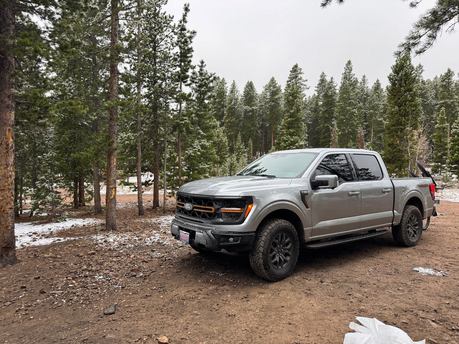 A grey Ford F-150 Tremor pickup truck sits in a snowy forest, ready for outdoor adventures like an RV rental.