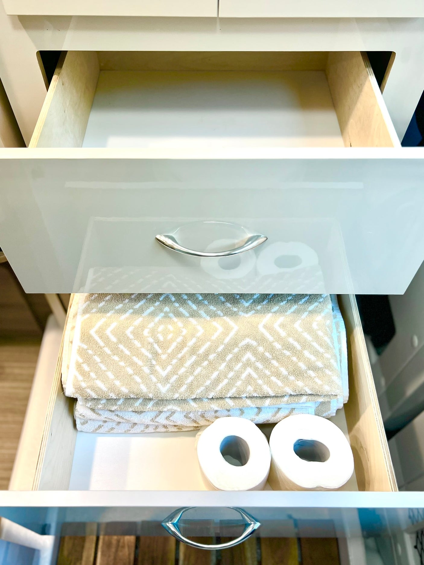 Organized RV rental drawers: clean towels & toilet paper ready in a bathroom vanity. Top drawers are empty.
