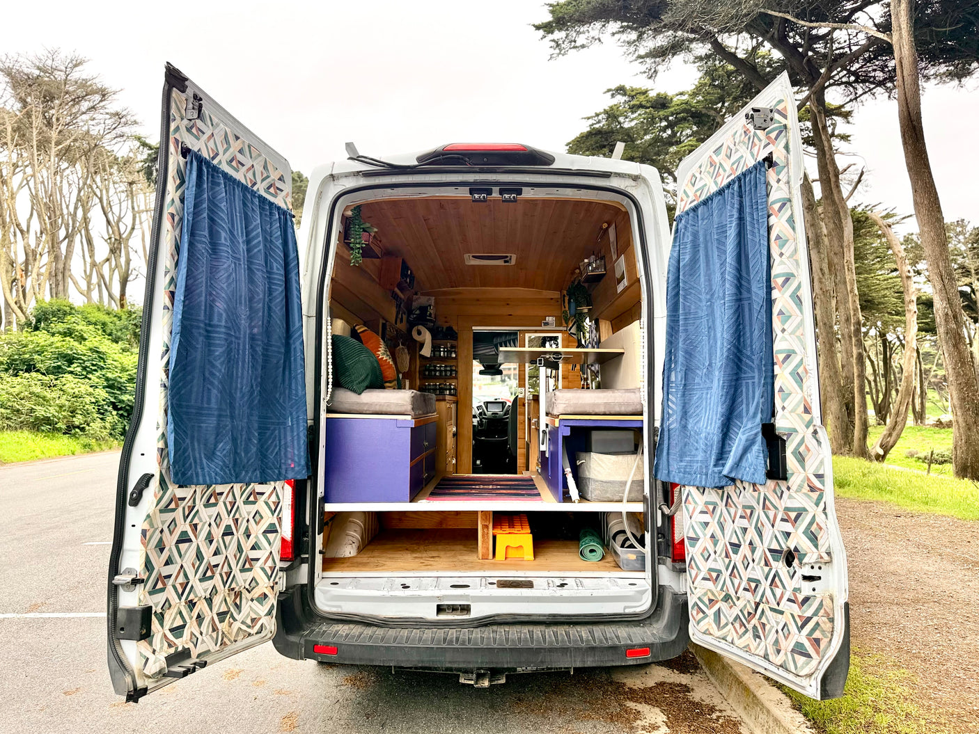 RV rental campervan with open rear doors showing its cozy interior setup amidst trees.