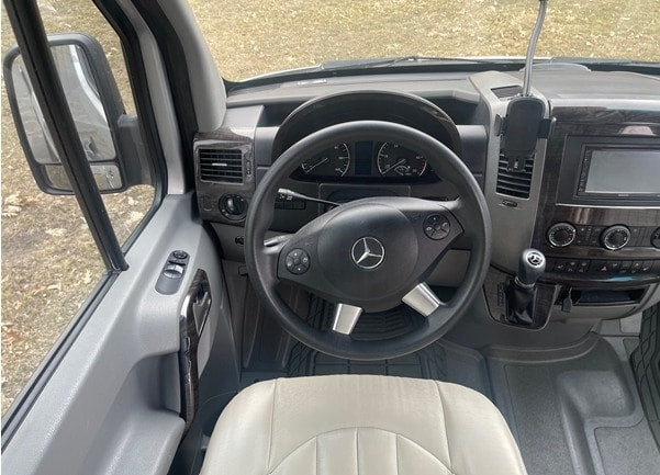 a large navigation screen displays a map above climate controls and a Mercedes-Benz shifter.|The driver's cockpit of an RV rental