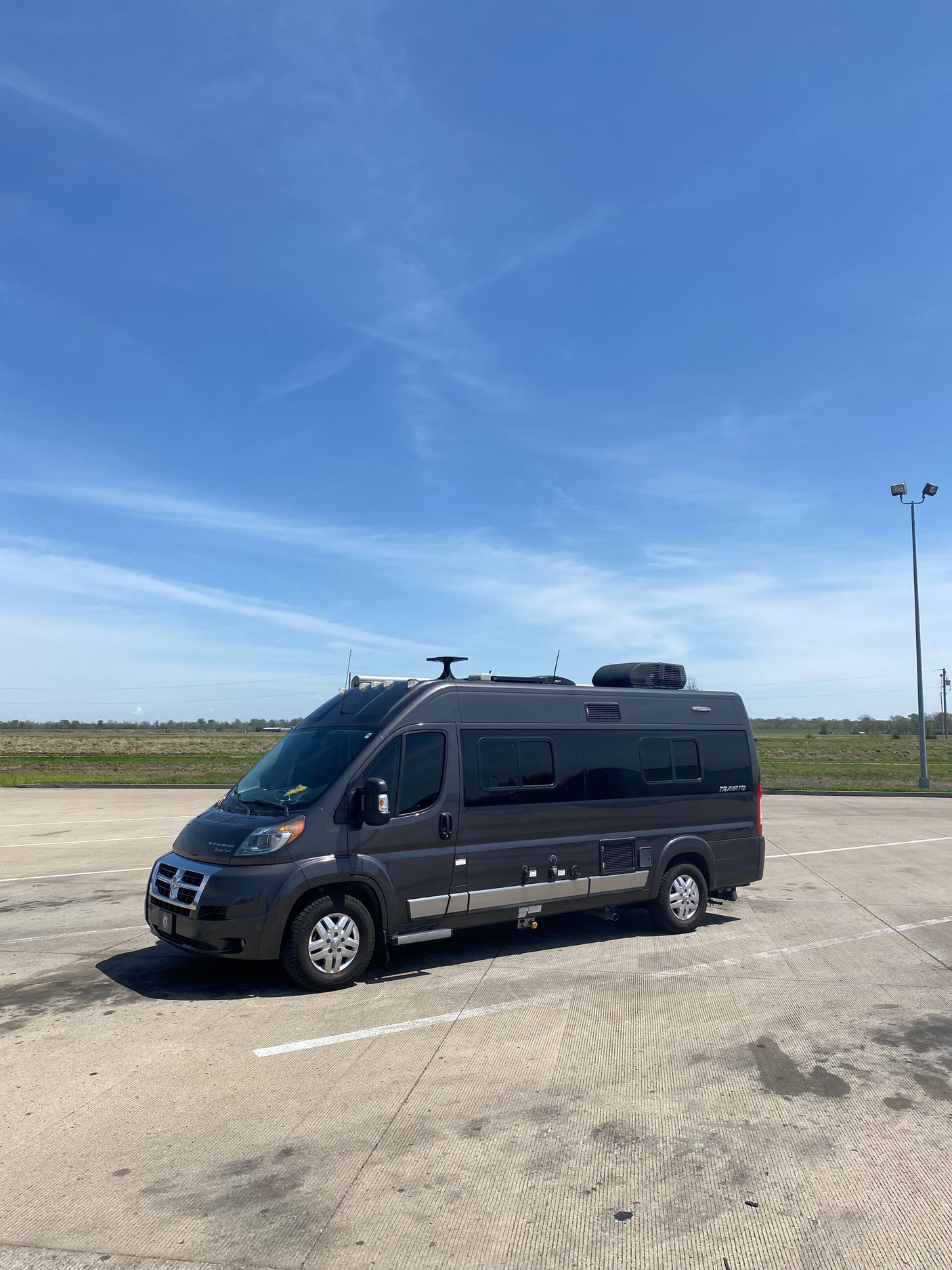 Dark grey Winnebago Travato RV rental parked on concrete under a bright blue sky, ready for travel.