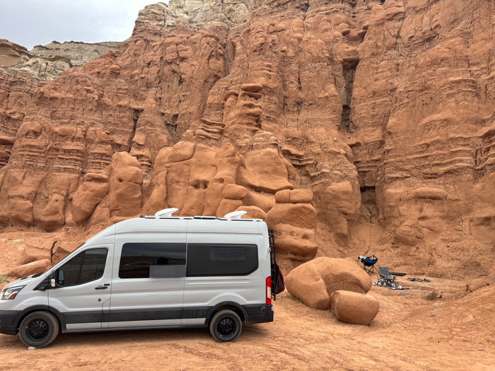 White RV rental camper van parked at a unique desert campsite amidst stunning red rock formations.