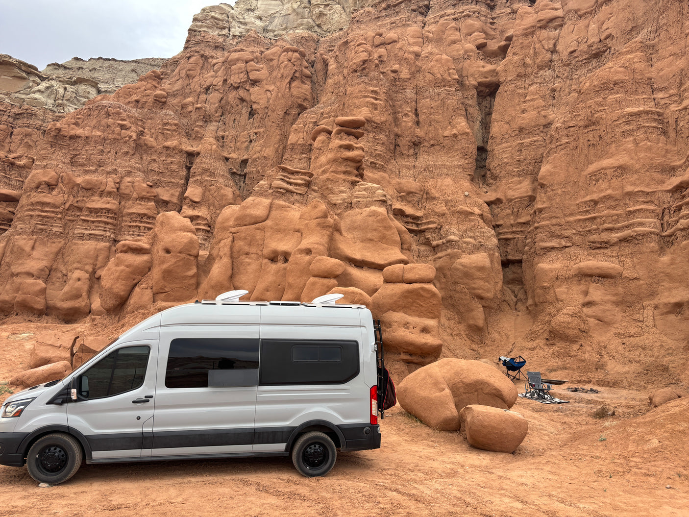 White RV rental camper van parked at a unique desert campsite amidst stunning red rock formations.