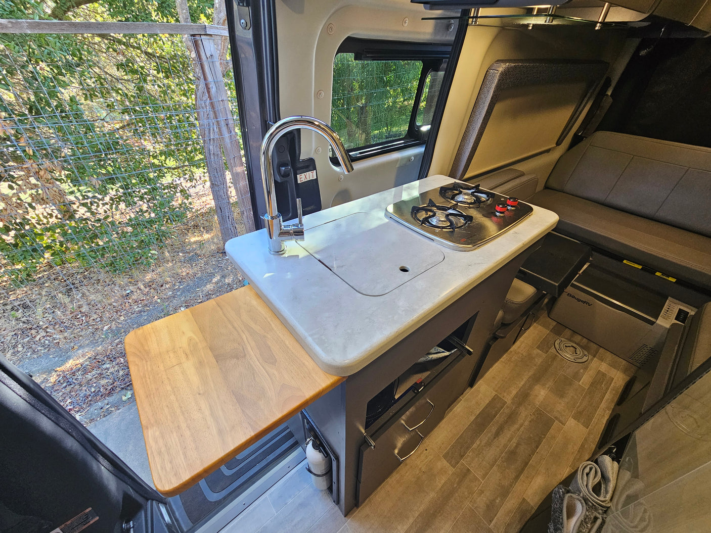 Inside this rv rental, a compact kitchen with a sink, two-burner stove, extendable counter, and convertible seating area.