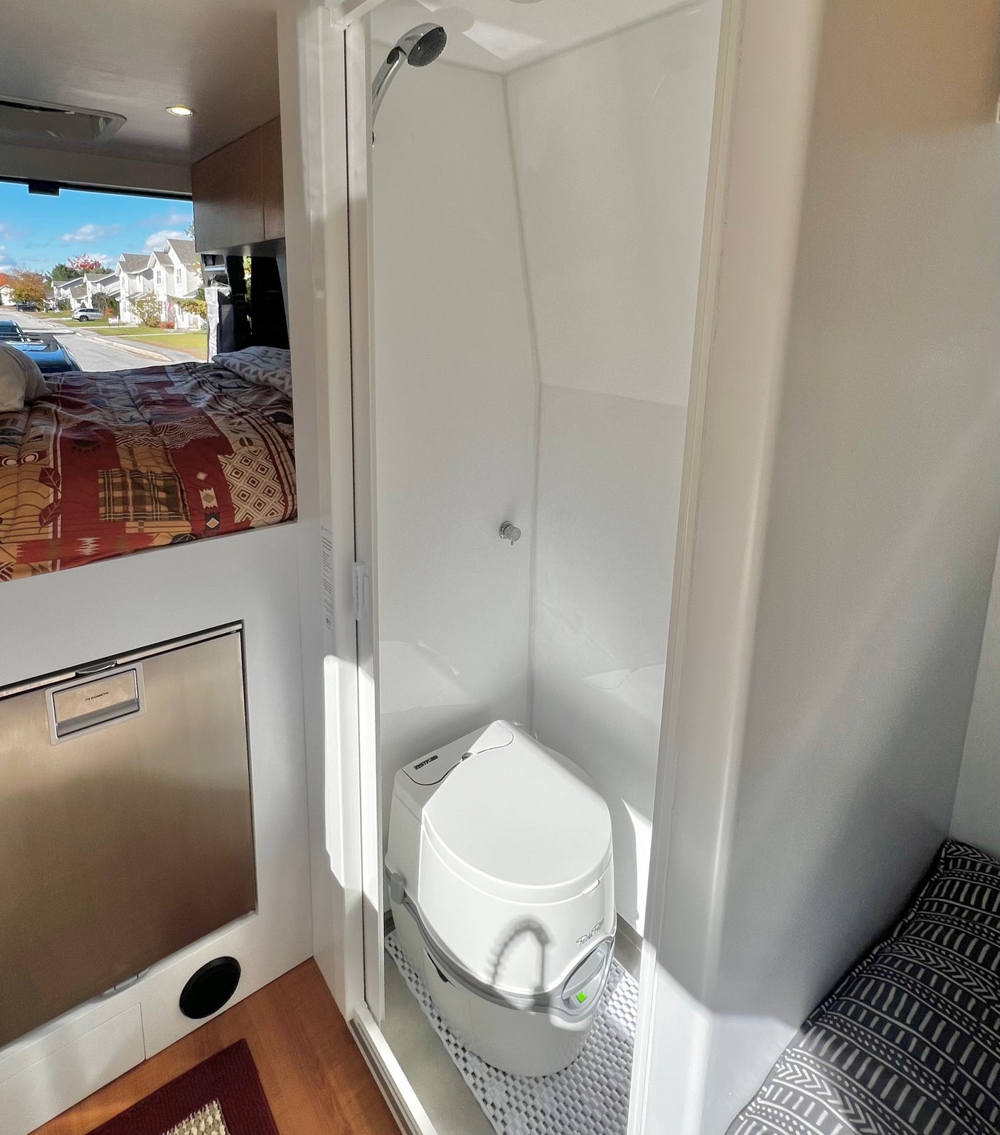 RV rental interior features a compact bed, refrigerator, and wet bath with shower & portable toilet.
