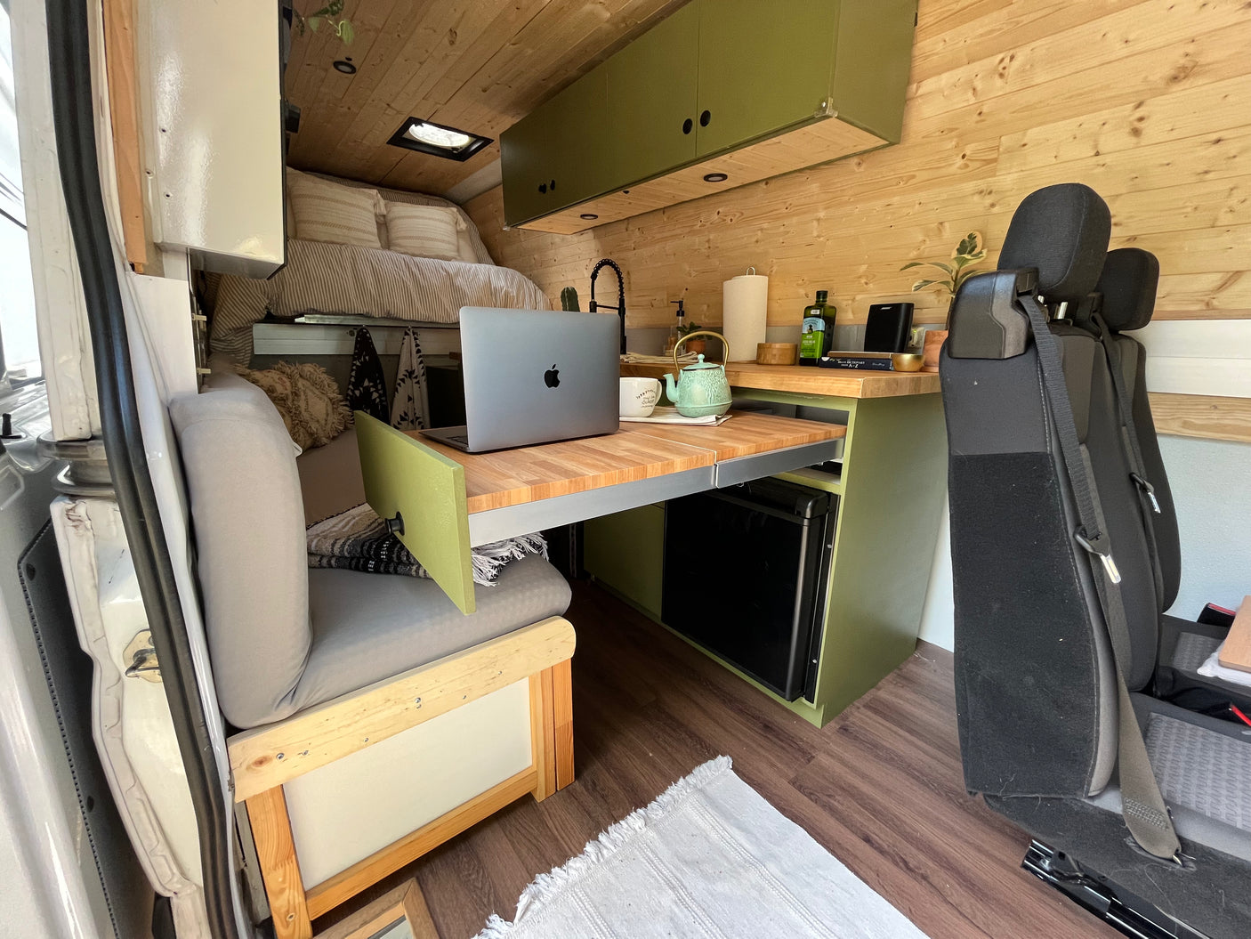 Inside a modern RV rental: wood-paneled camper van with a cozy bed, compact kitchen, and a pull-out laptop workspace.