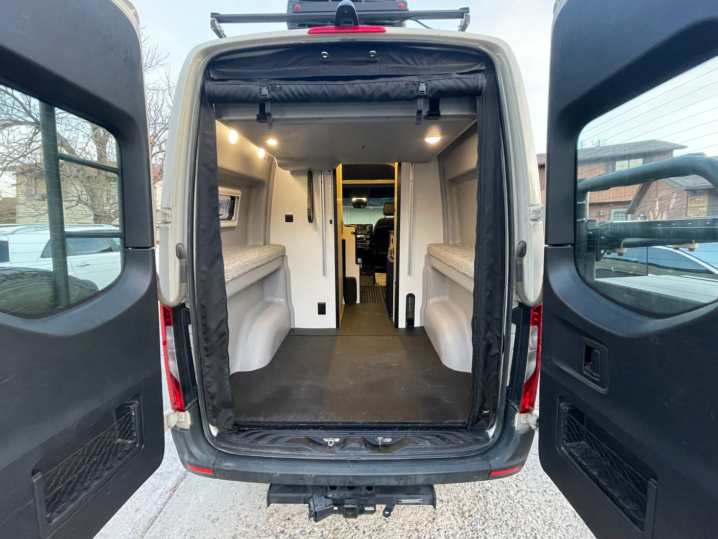 Rear view of this custom rv rental camper van, doors open to reveal its organized interior with sleeping platforms and storage.