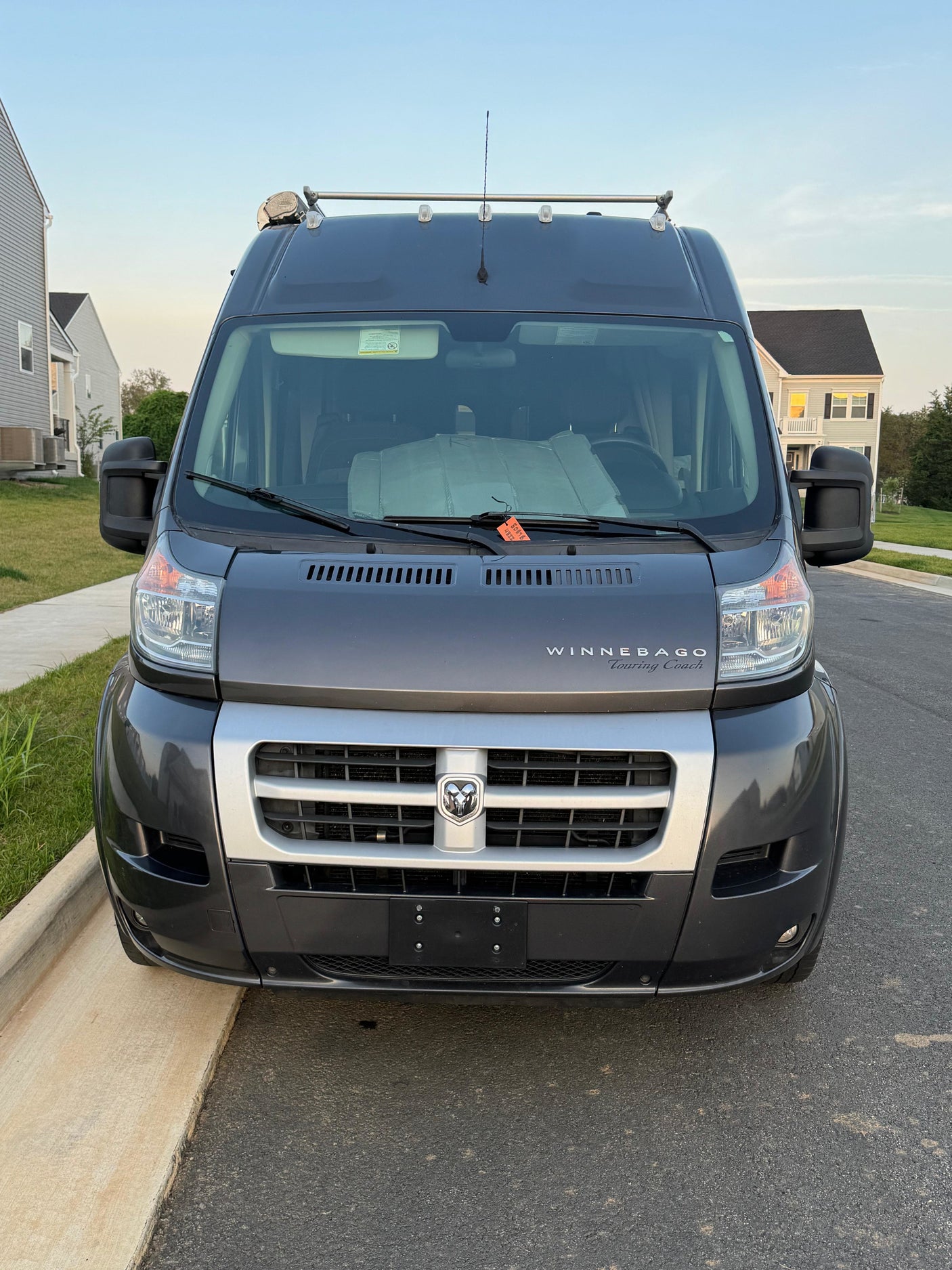 Front view of a dark grey Winnebago Touring Coach RV rental, featuring a Dodge Ram logo, roof racks, and sunshade.
