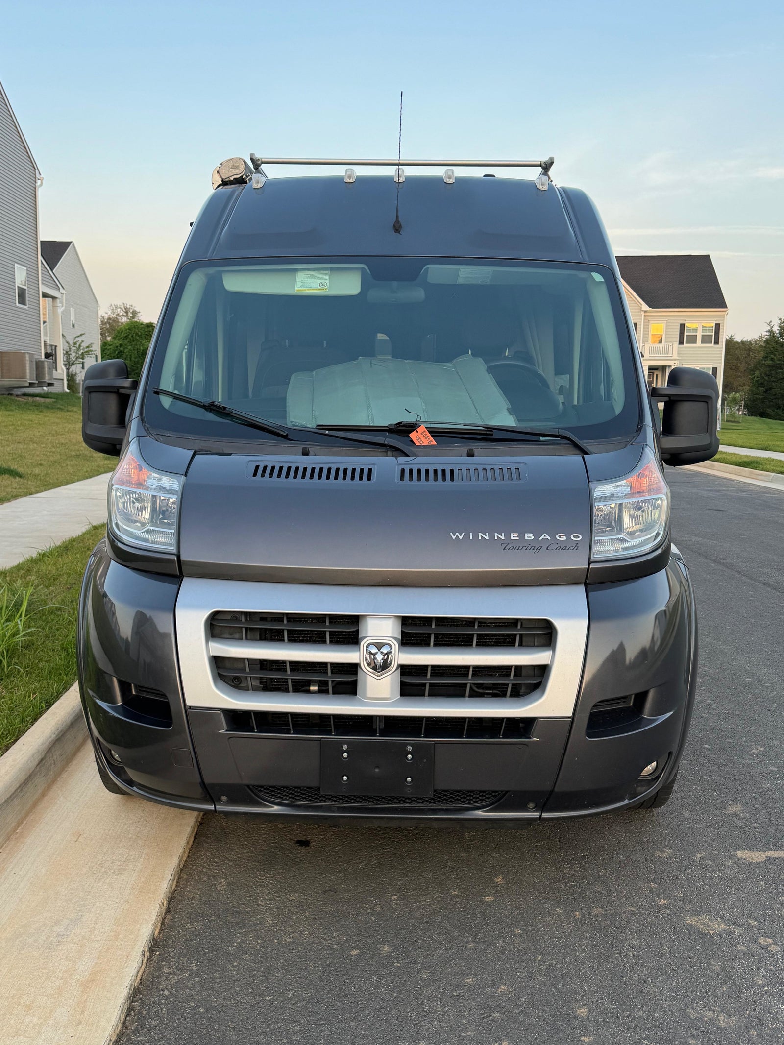 Front view of a dark grey Winnebago Touring Coach RV rental, featuring a Dodge Ram logo, roof racks, and sunshade.