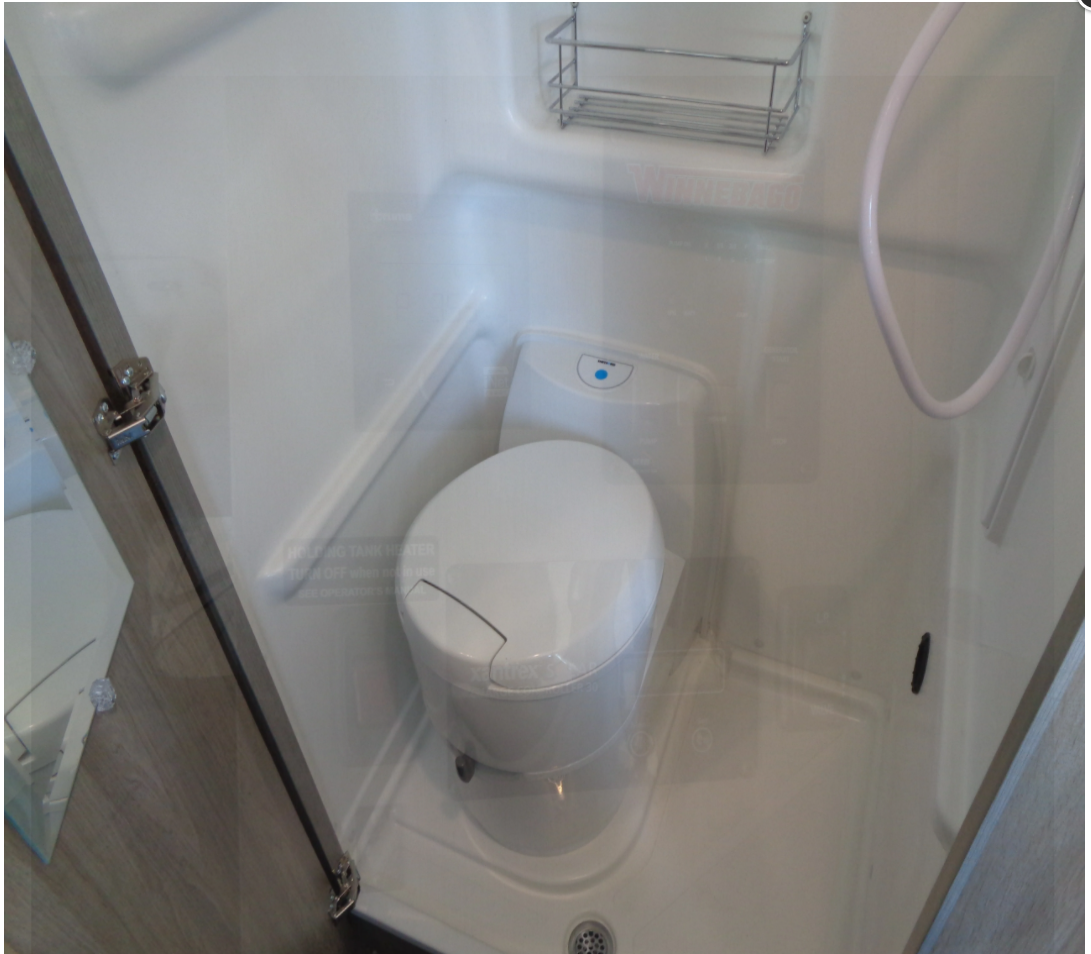 This compact RV rental bathroom includes a white toilet, shower head, and small wall-mounted shelf.
