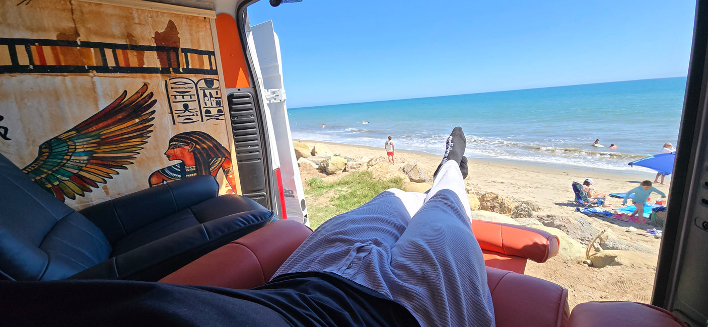 Relaxing in an rv rental! Legs up, enjoying the sunny beach view with clear blue sea and people from a van with Egyptian decor.