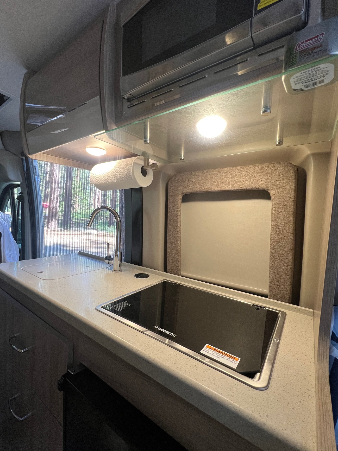 Modern RV rental kitchen with a Dometic cooktop, sink, and microwave. Brightly lit, ready for camping adventures.