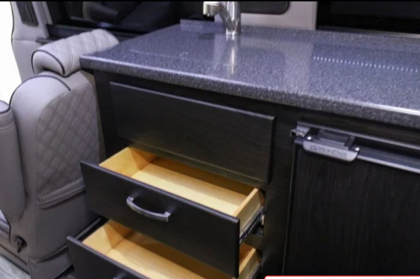 RV rental interior: Modern kitchen with dark cabinets, open drawers, sink, fridge, and luxury seating visible. — photo 16