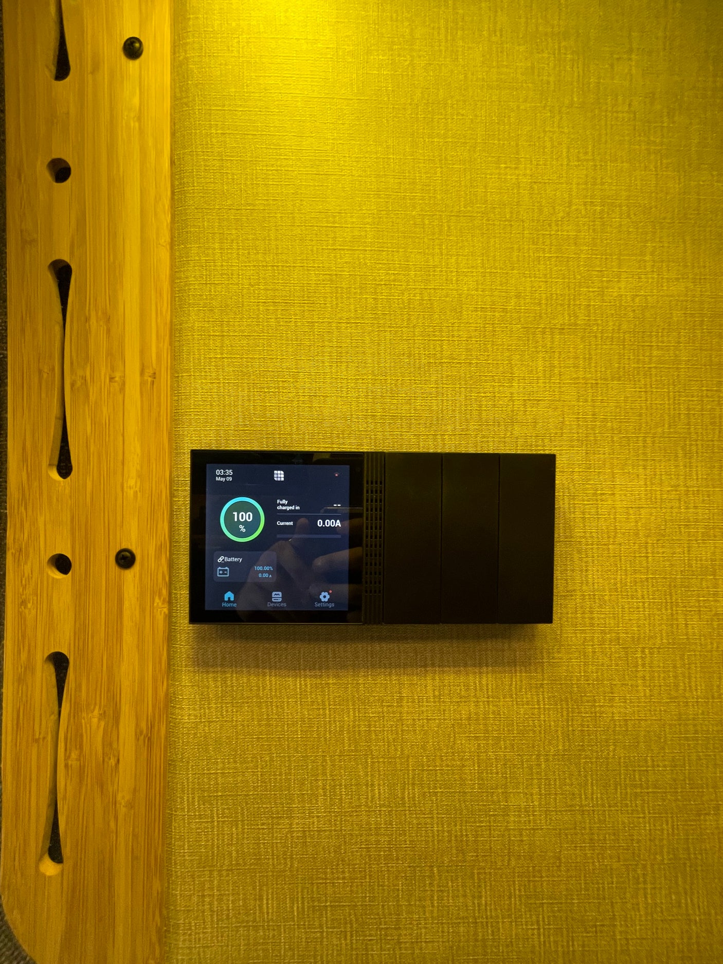 RV rental: Digital control panel displaying 100% battery charge and current status in an RV, mounted on a textured wall.