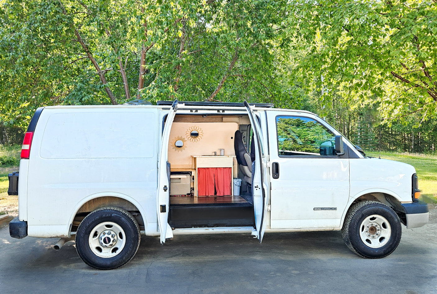 Converted white GMC van with open doors, revealing its cozy, custom interior with a sink and decorative mirrors, ideal for RV rental.
