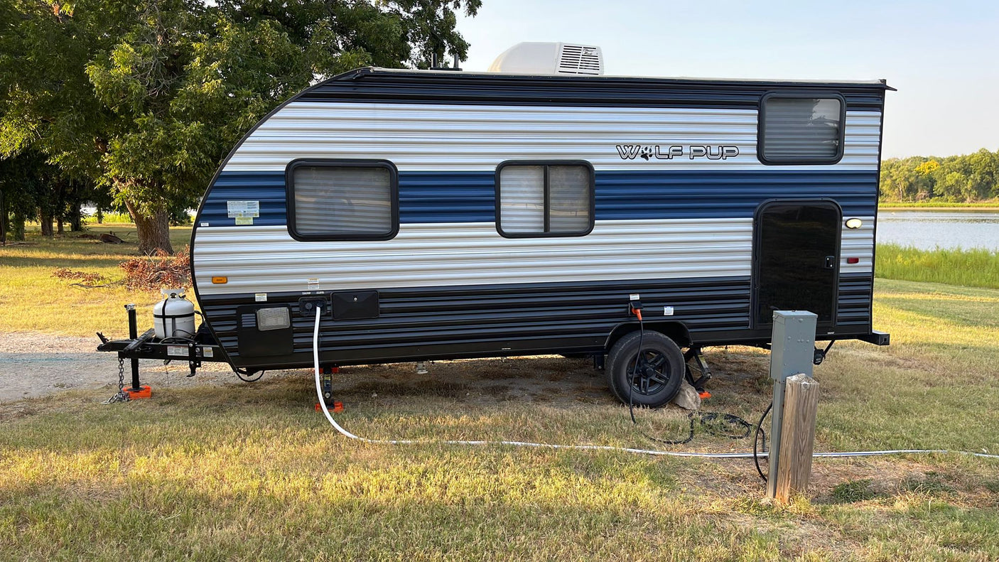 Experience nature with this RV rental. A travel trailer is set up lakeside with utilities, perfect for camping and outdoor travel.