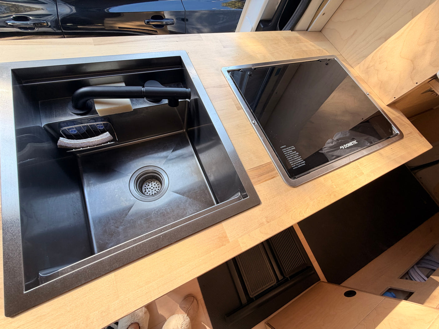 This RV rental kitchen features a sleek stainless steel sink with a black faucet and a Dometic glass cooktop on a wood counter.