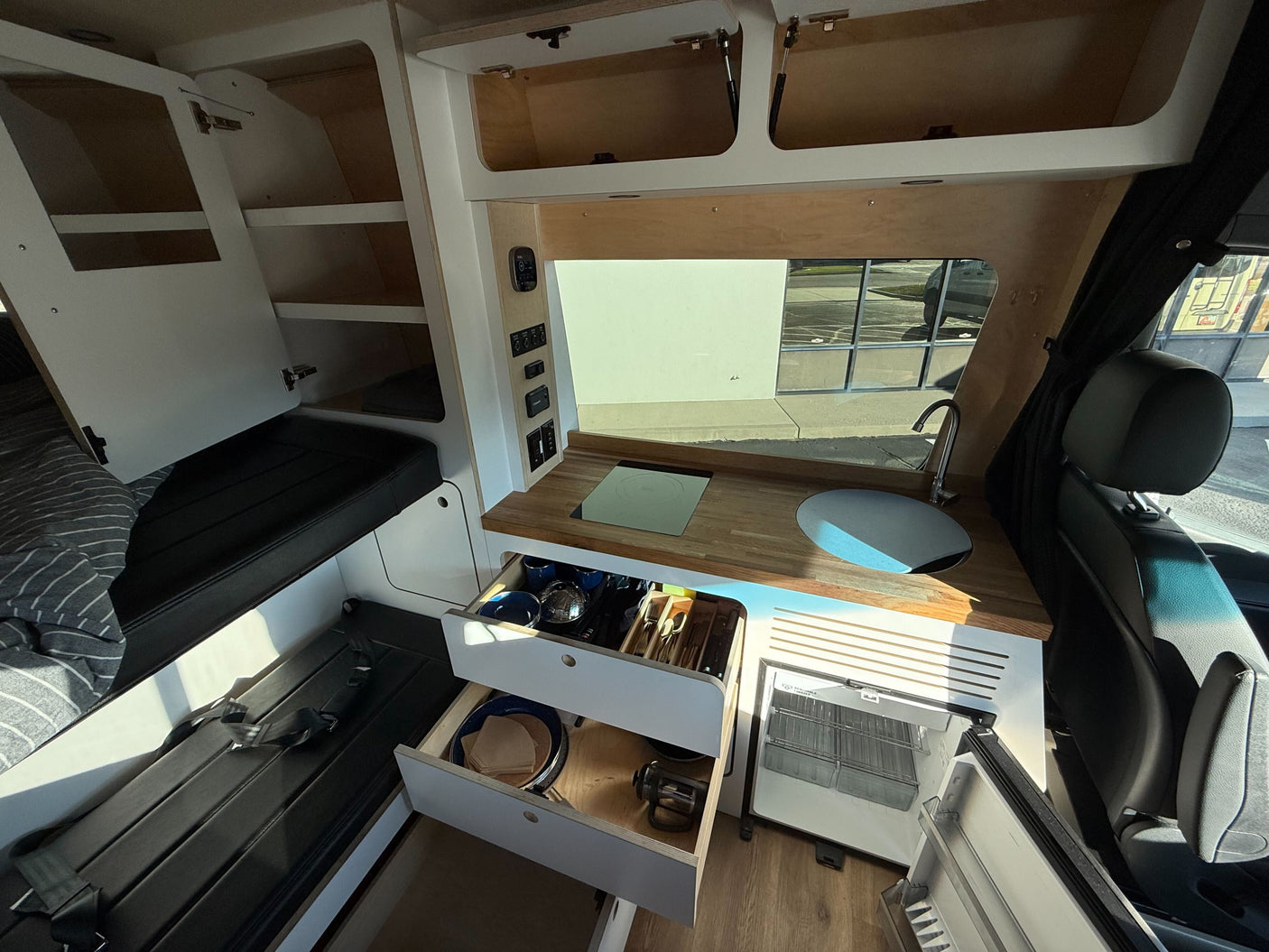 RV rental interior: cozy camper van with kitchenette, open drawers, fridge, and built-in storage.