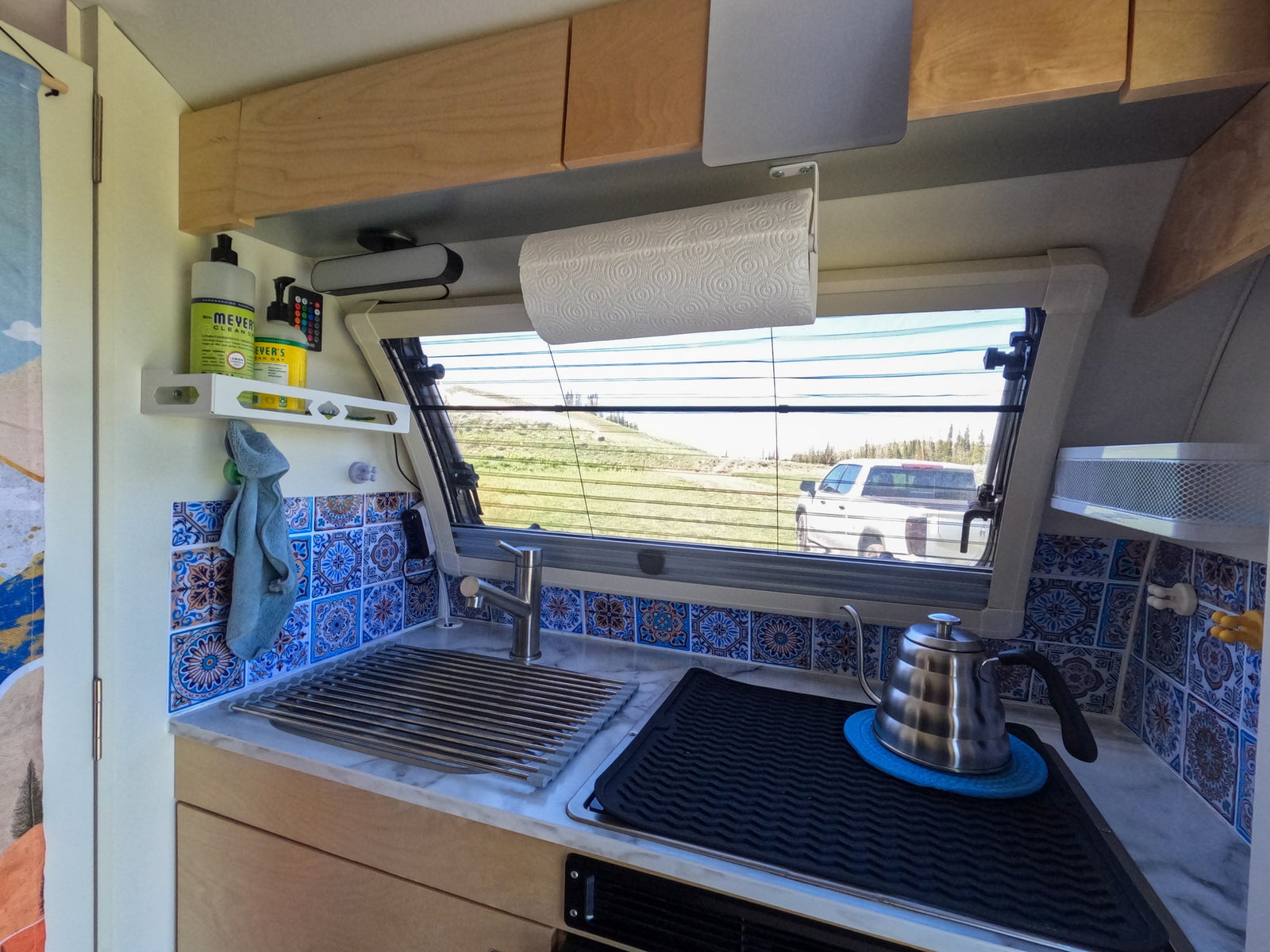 This RV rental's compact kitchen features a sink, kettle, tiled backsplash, and a window with outdoor views.