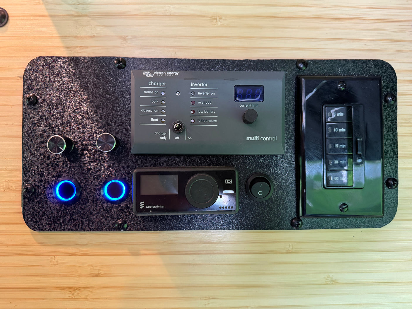 RV rental power control panel: Victron Energy Multi Control, Eberspächer heater, and timer switches mounted on wood.