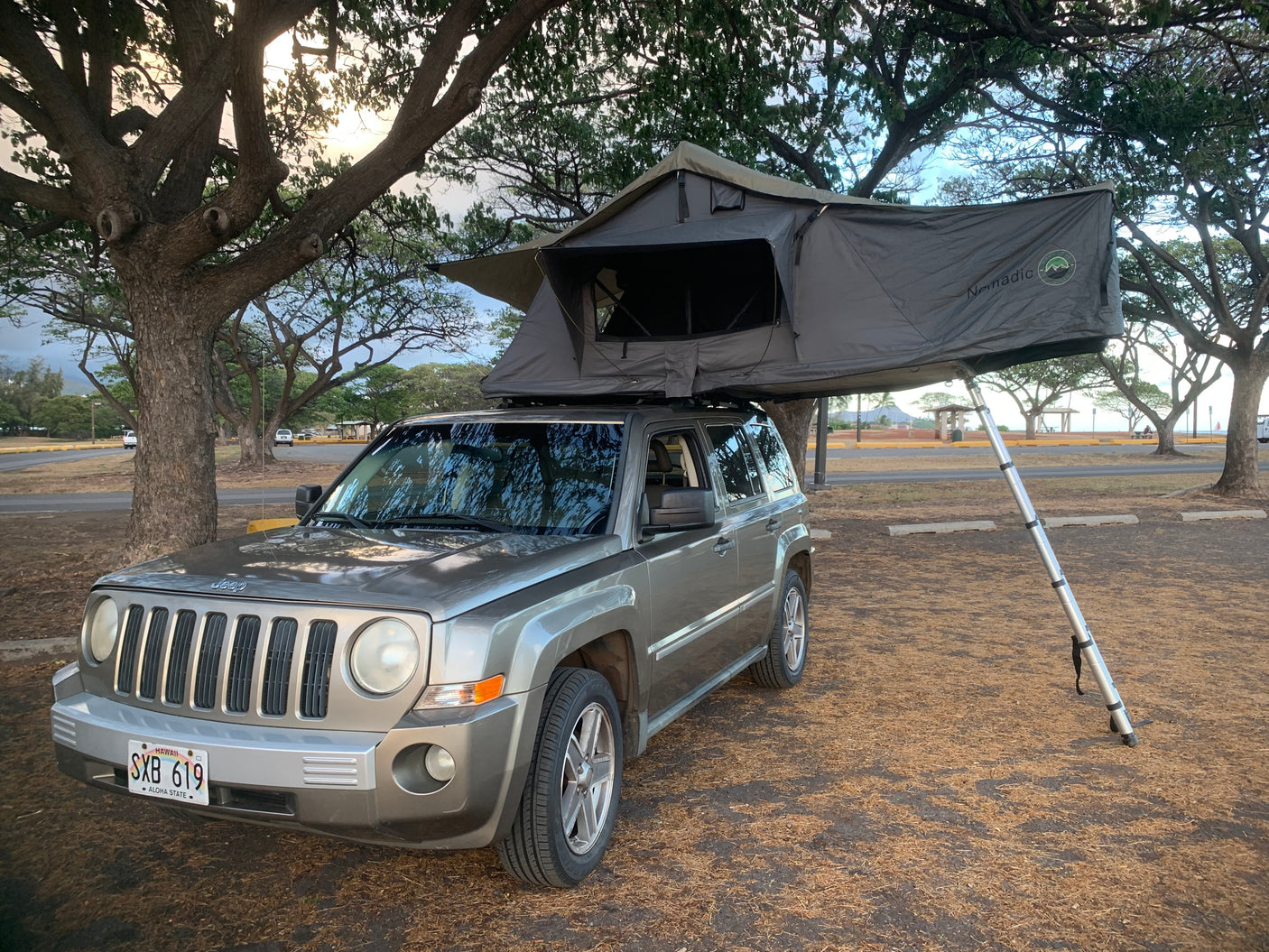 A grey Jeep Patriot SUV with a deployed Nomadic rooftop tent, an RV rental alternative for outdoor adventures.