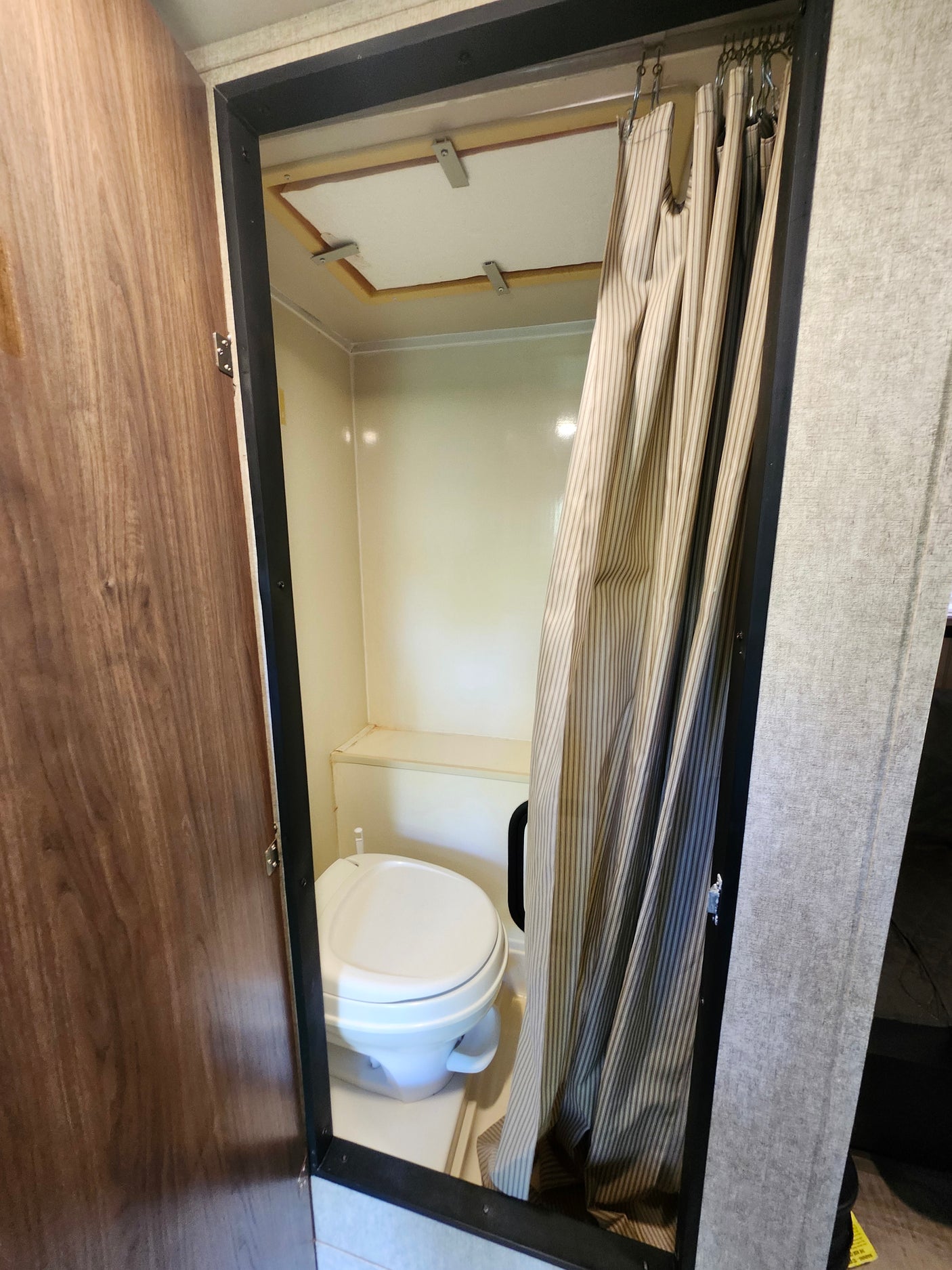 Compact RV rental bathroom with a white toilet, striped shower curtain, and ceiling panel. Practical for travel.