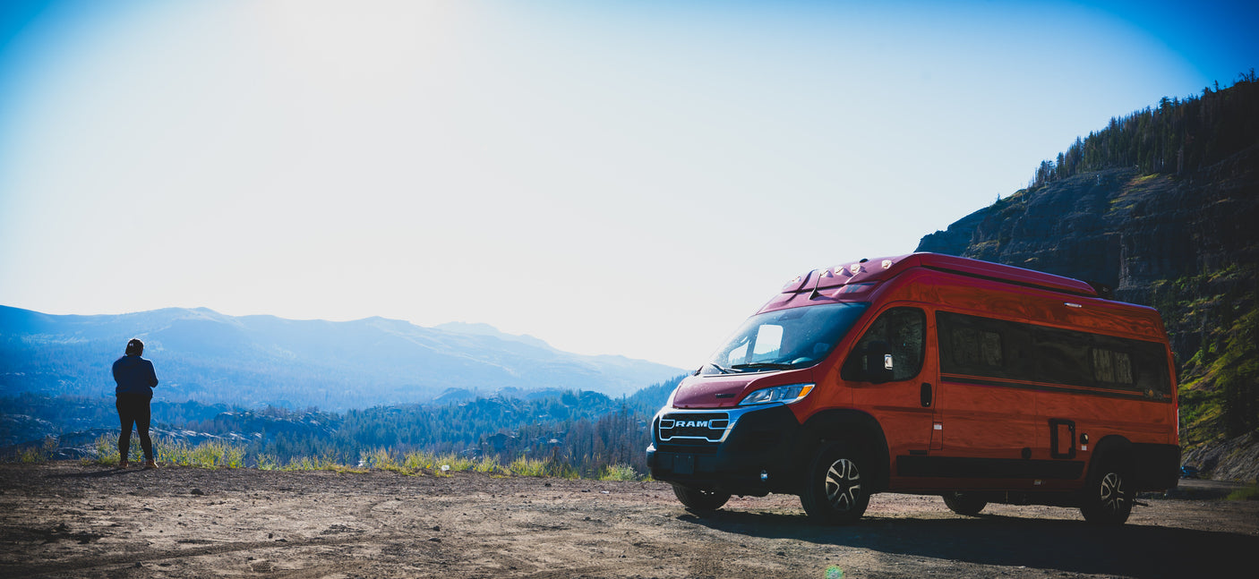 Adventure awaits: Red RV rental parked at a scenic overlook, person enjoys mountain views.
