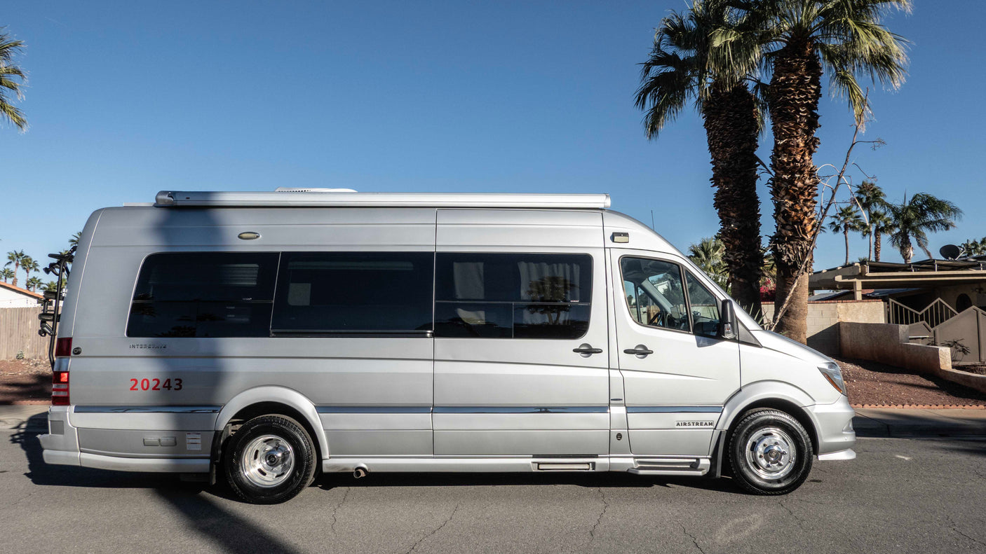 Silver van-style Airstream rv rental, with palm trees under a clear blue sky. Perfect for your next adventure.