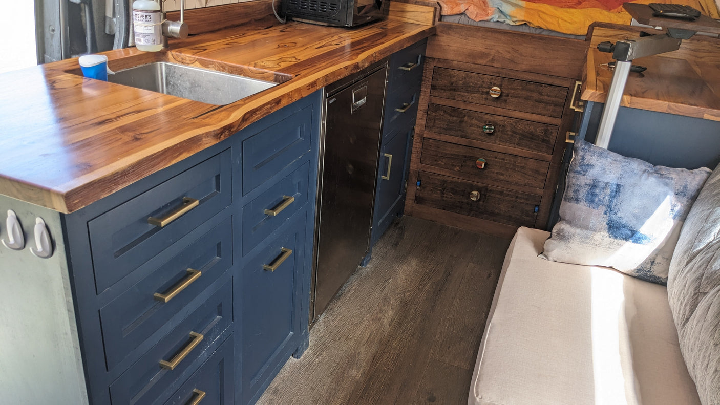 Inside this RV rental, discover a chic kitchen with live-edge wood counters, blue cabinets, built-in fridge, and a cozy lounge area.