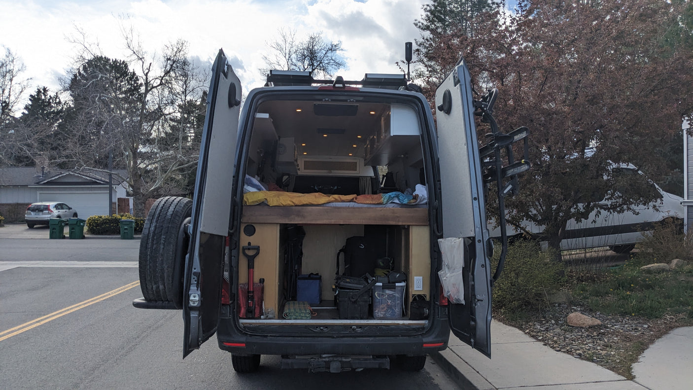 Rear view of a customized camper van with open doors, revealing a cozy bed and ample storage. Book your RV rental adventure!
