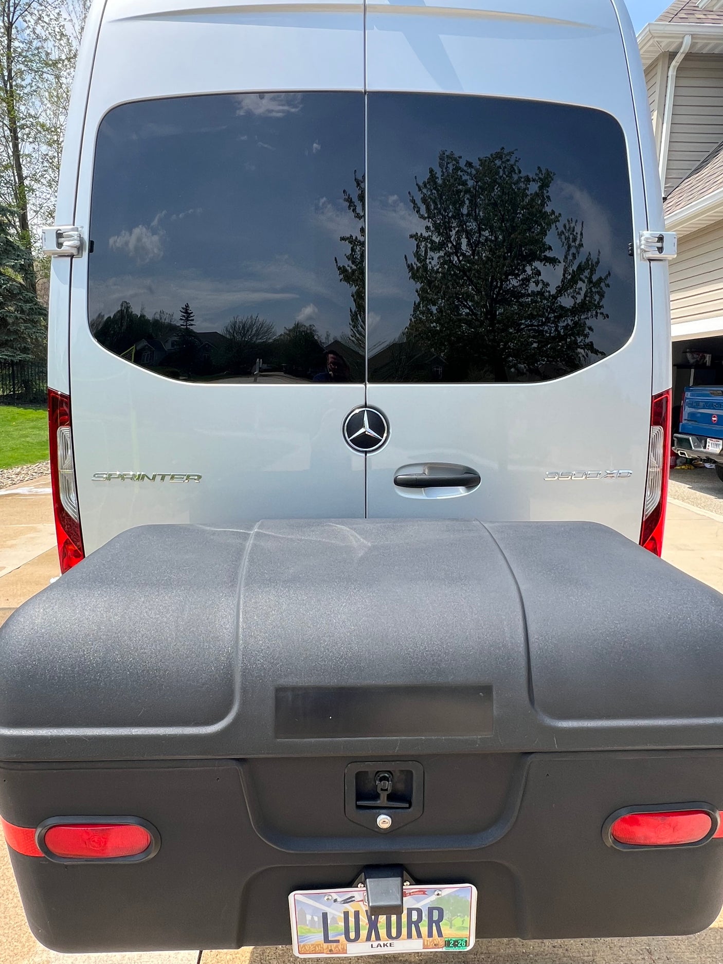 Rear of silver Mercedes Sprinter van with large black cargo box & custom 'LUXURR' plate. An excellent rv rental option.