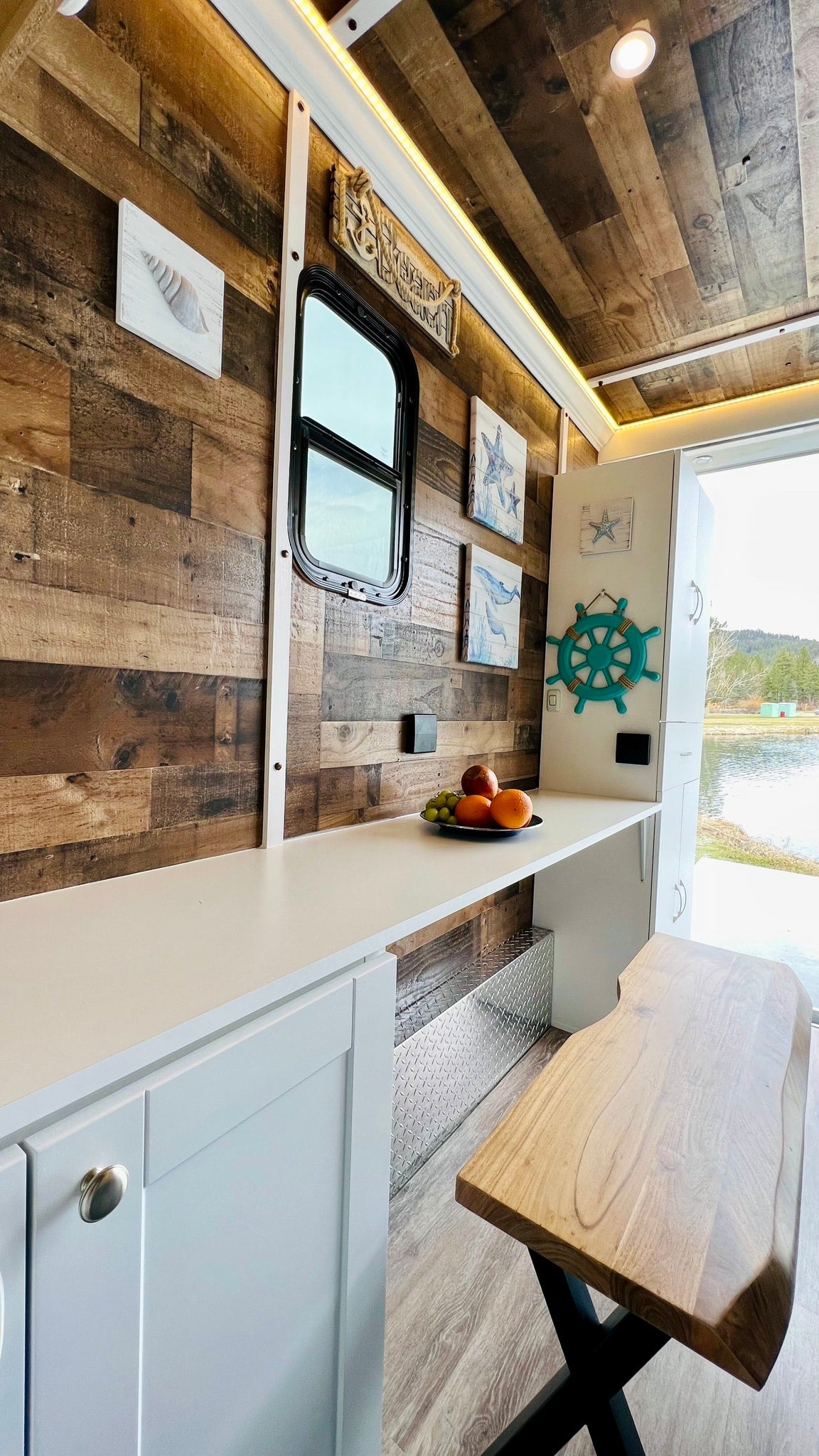 Cozy RV rental interior with rustic wood walls, coastal decor, functional counter, and scenic lake views for glamping.