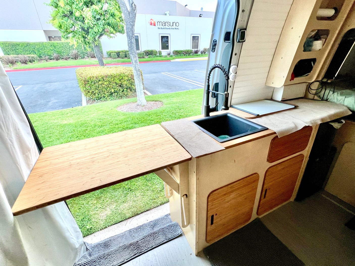 Inside this RV rental, a compact kitchen with sink and extendable counter opens to an outdoor view, perfect for mobile adventures.