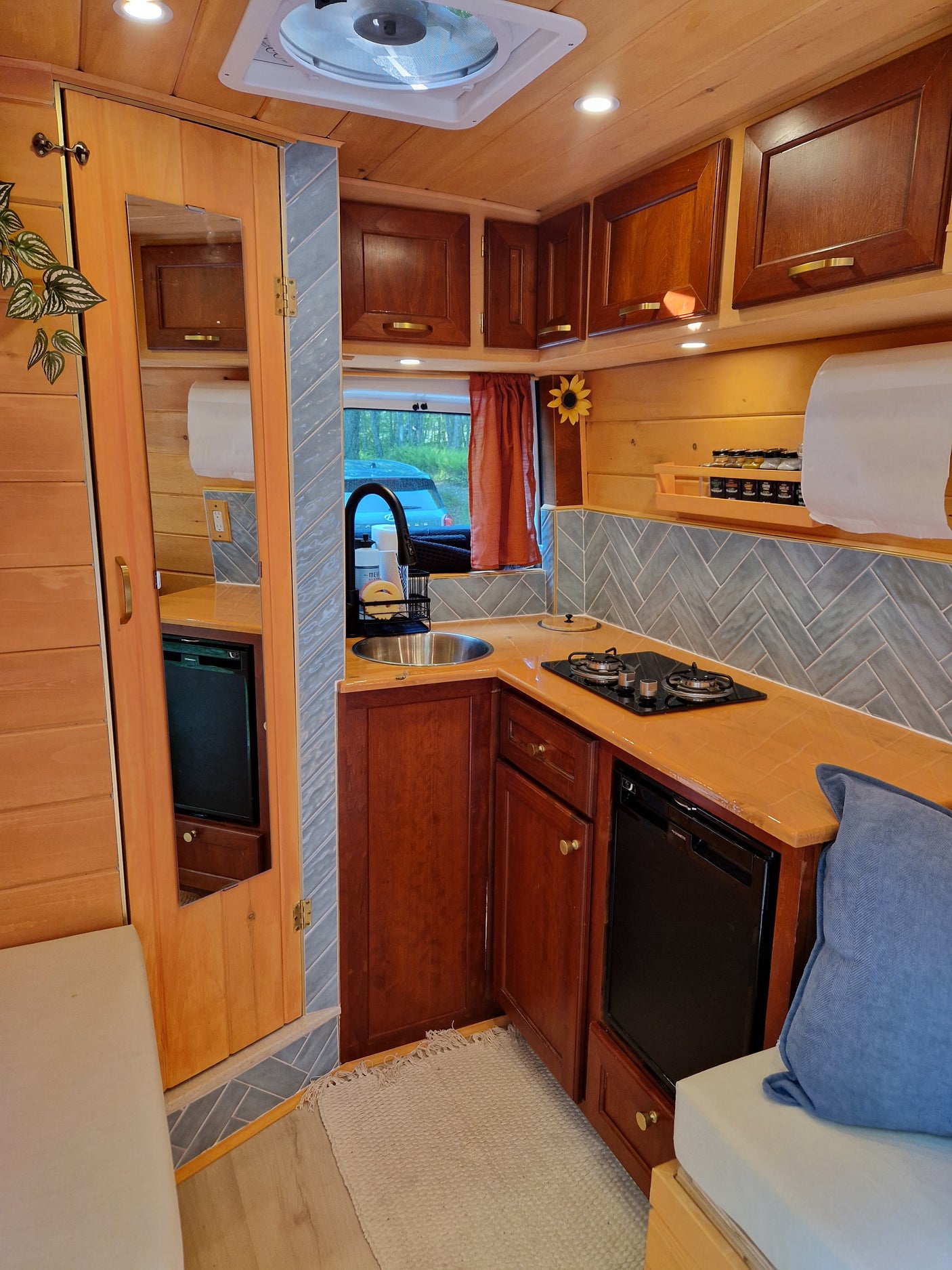 Cozy RV rental interior with a fully equipped kitchen featuring wood finishes, tiled backsplash, and compact appliances.