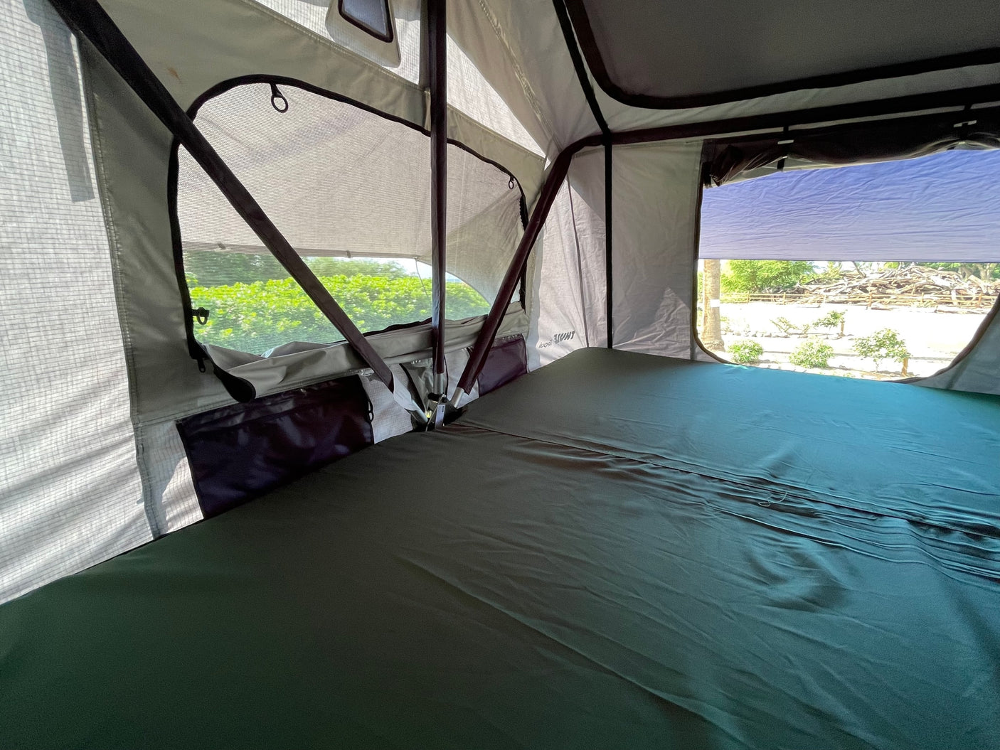 Inside an RV rental's rooftop tent, featuring a comfortable bed, mesh windows, and outdoor views.