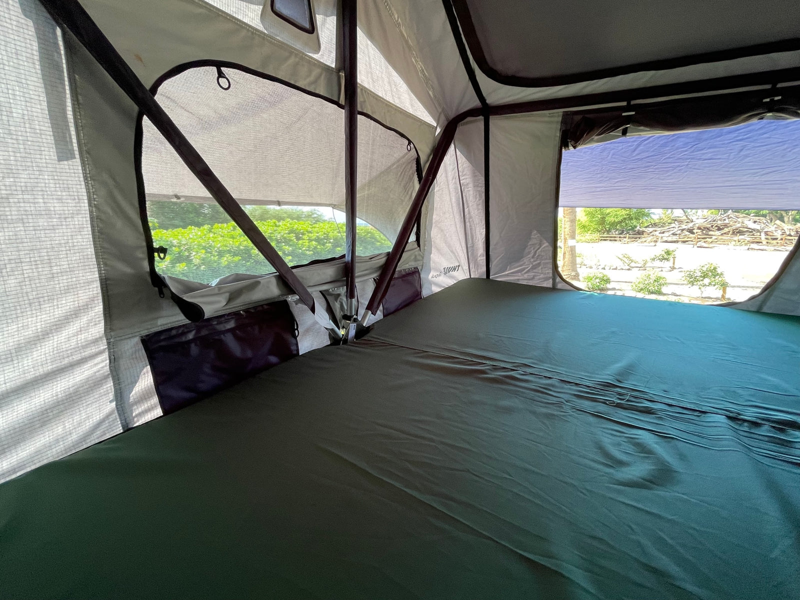 Inside an RV rental's rooftop tent, featuring a comfortable bed, mesh windows, and outdoor views.