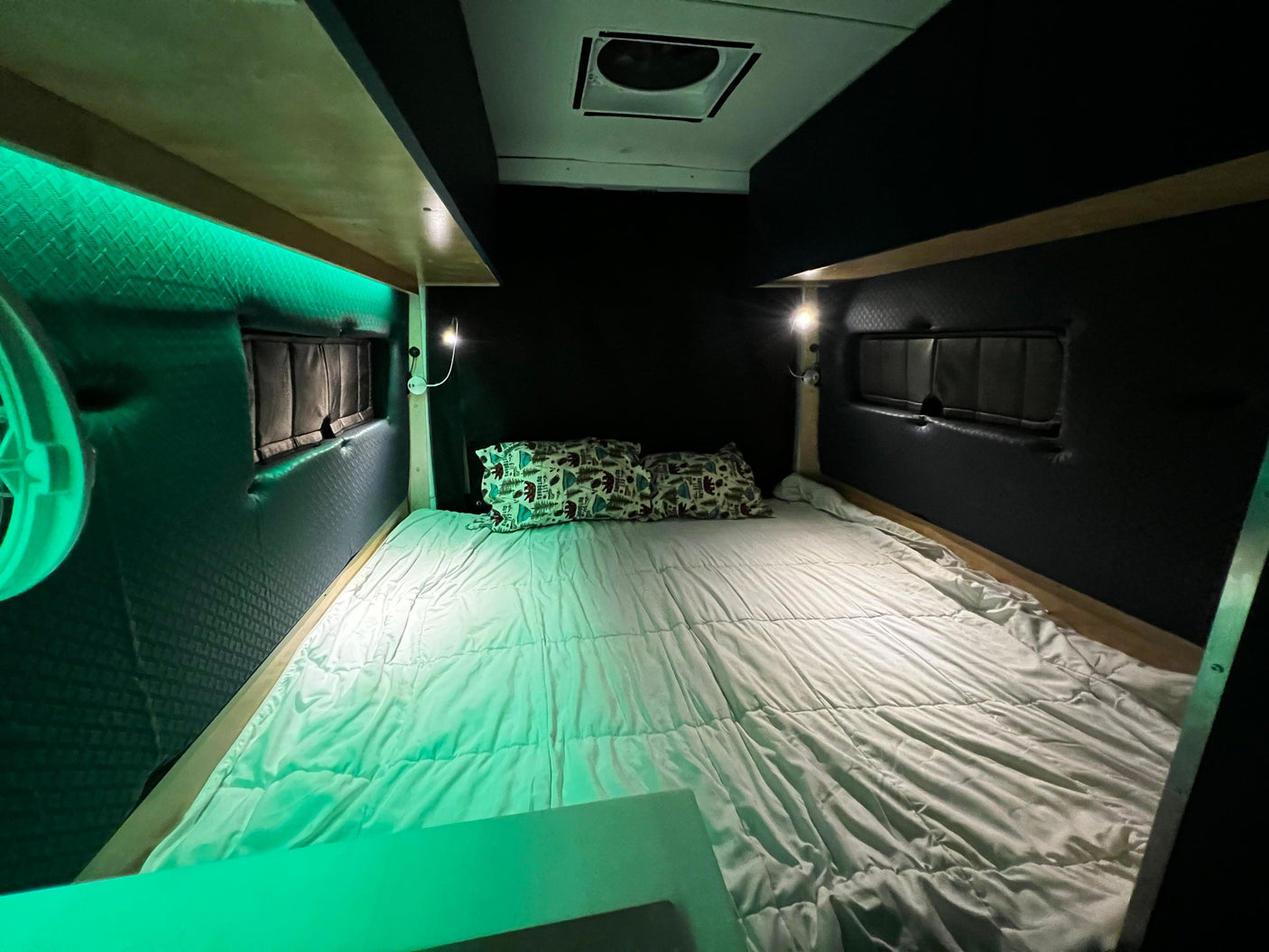 Cozy RV rental bed area featuring green LED accent lighting, individual reading lights, and nature-themed pillows.