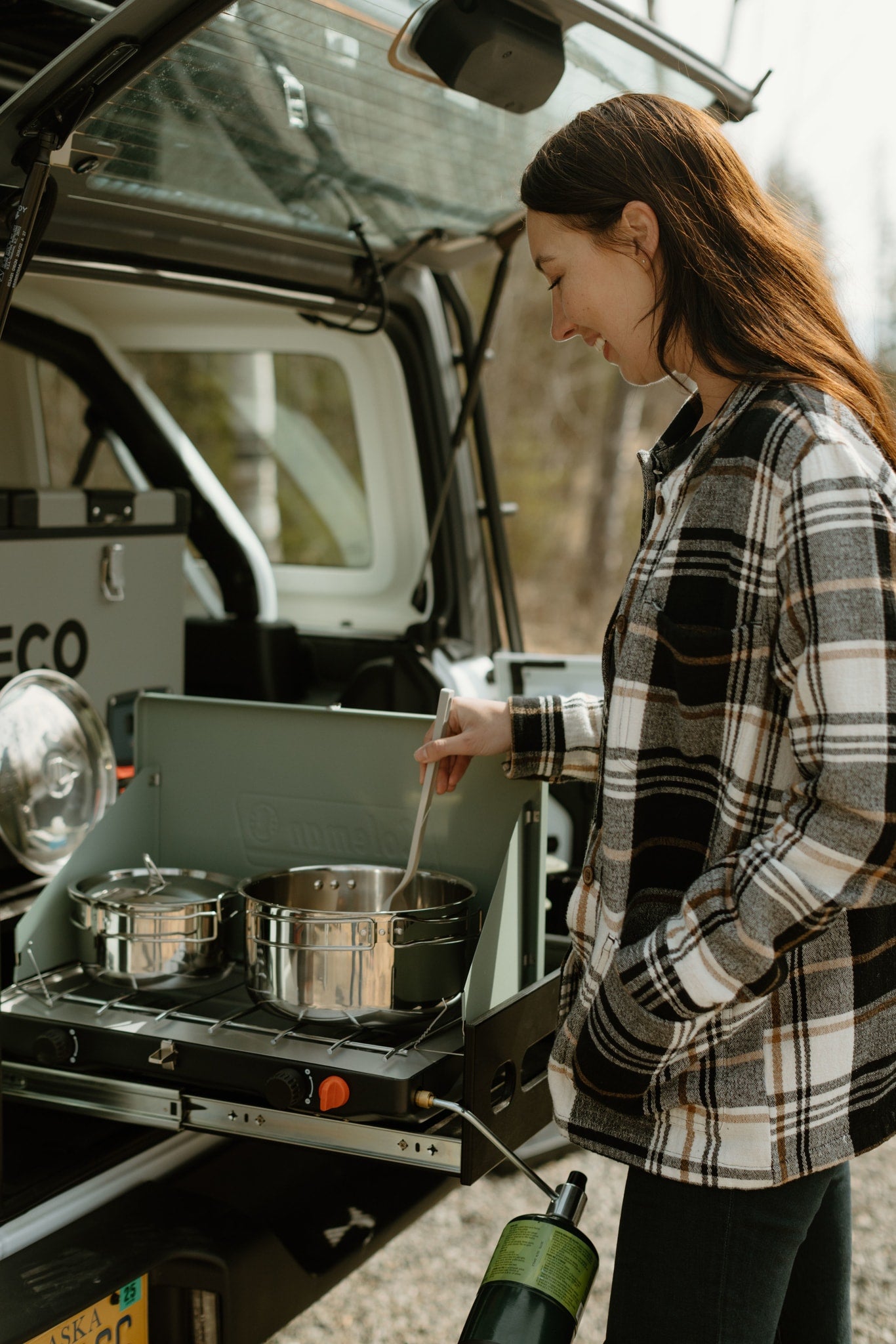 A woman prepares a meal using a camp stove pulled from her RV rental, highlighting the convenience of outdoor cooking.