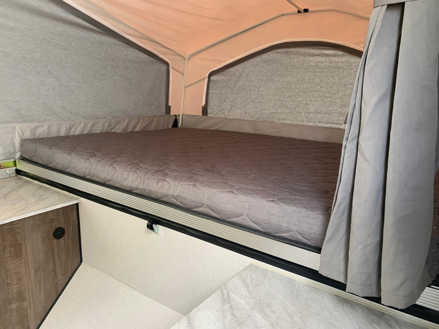 Cozy pop-up camper bed in an RV rental, featuring a quilted mattress, privacy curtain, and convenient USB charging port.
