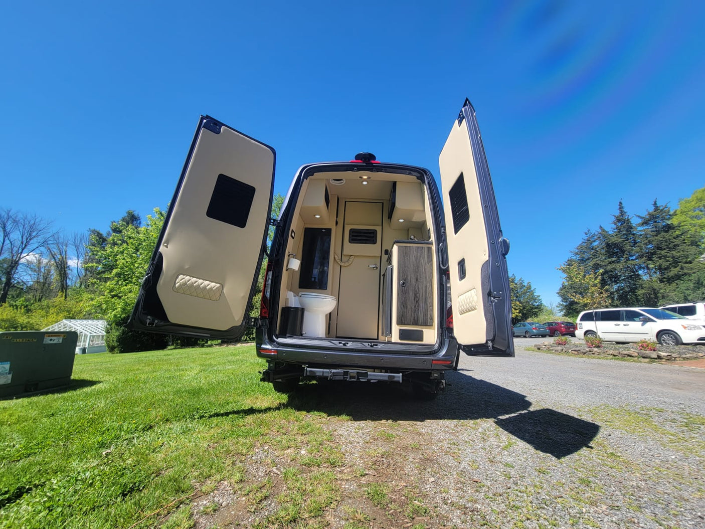 Explore this RV rental's spacious interior! Rear doors open, revealing a built-in toilet & kitchenette, perfect for road trips.