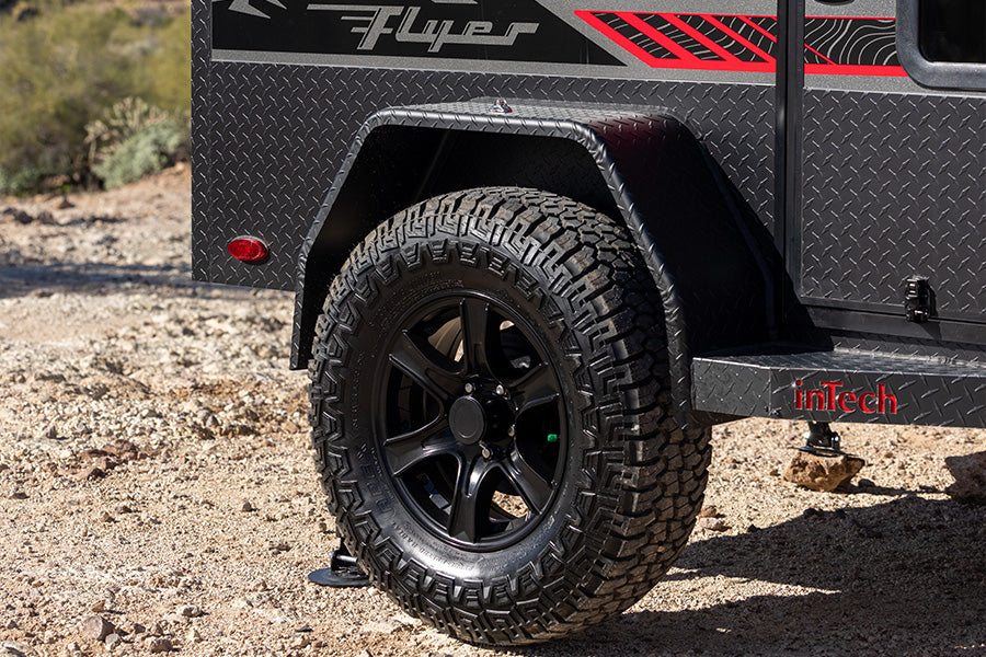 Close-up of a rugged off-road rv rental trailer's wheel, highlighting its all-terrain tire and diamond plate body.