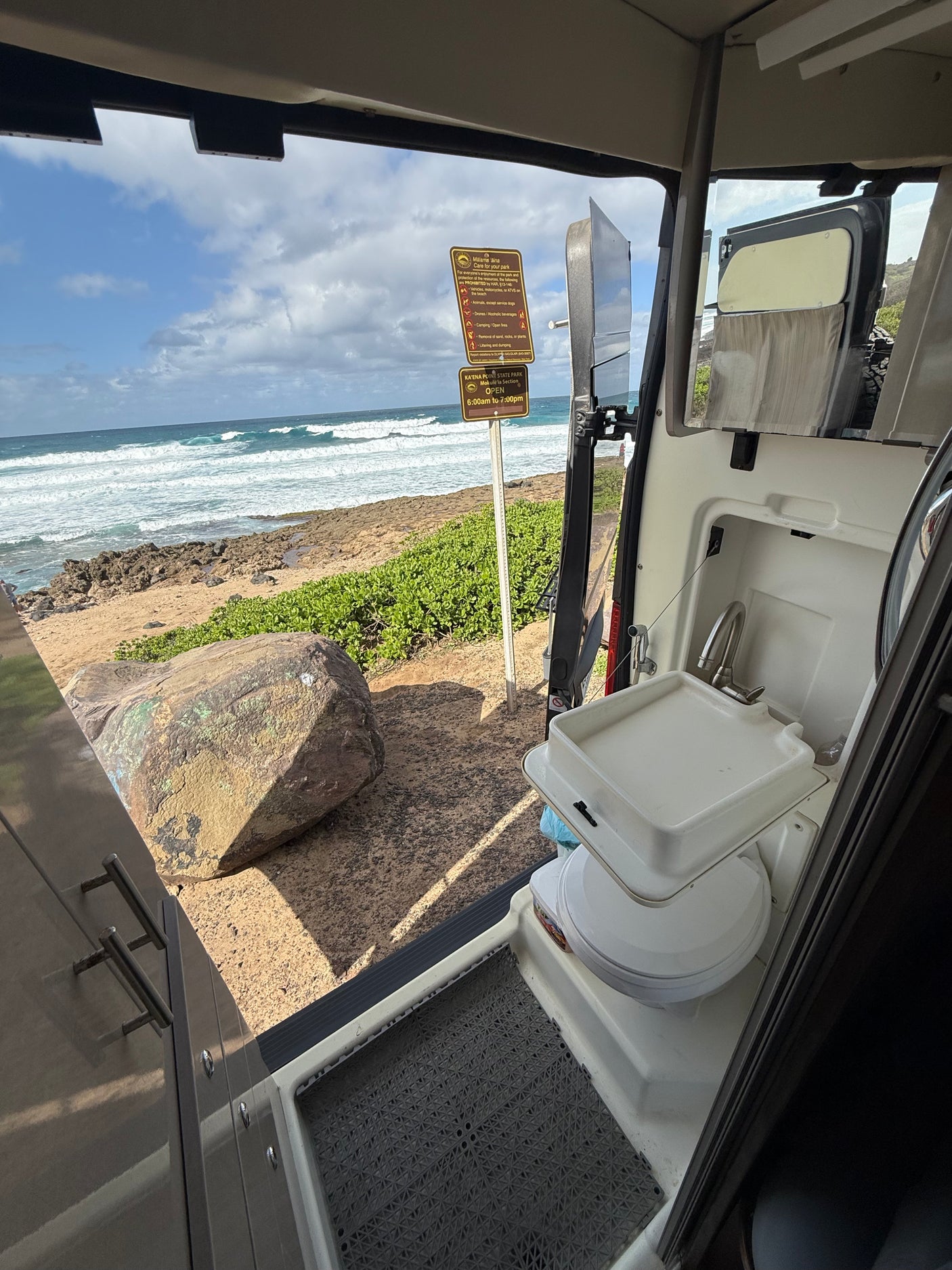An **rv rental** interior shows a sink and toilet, with an open door view of the ocean waves and a Ka'ena Point **State Park** sign.