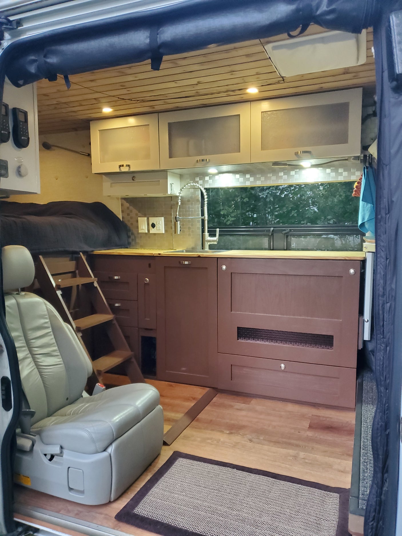 RV rental interior: Elevated bed with ladder, full kitchenette, and a comfortable swiveling seat in a cozy camper van.