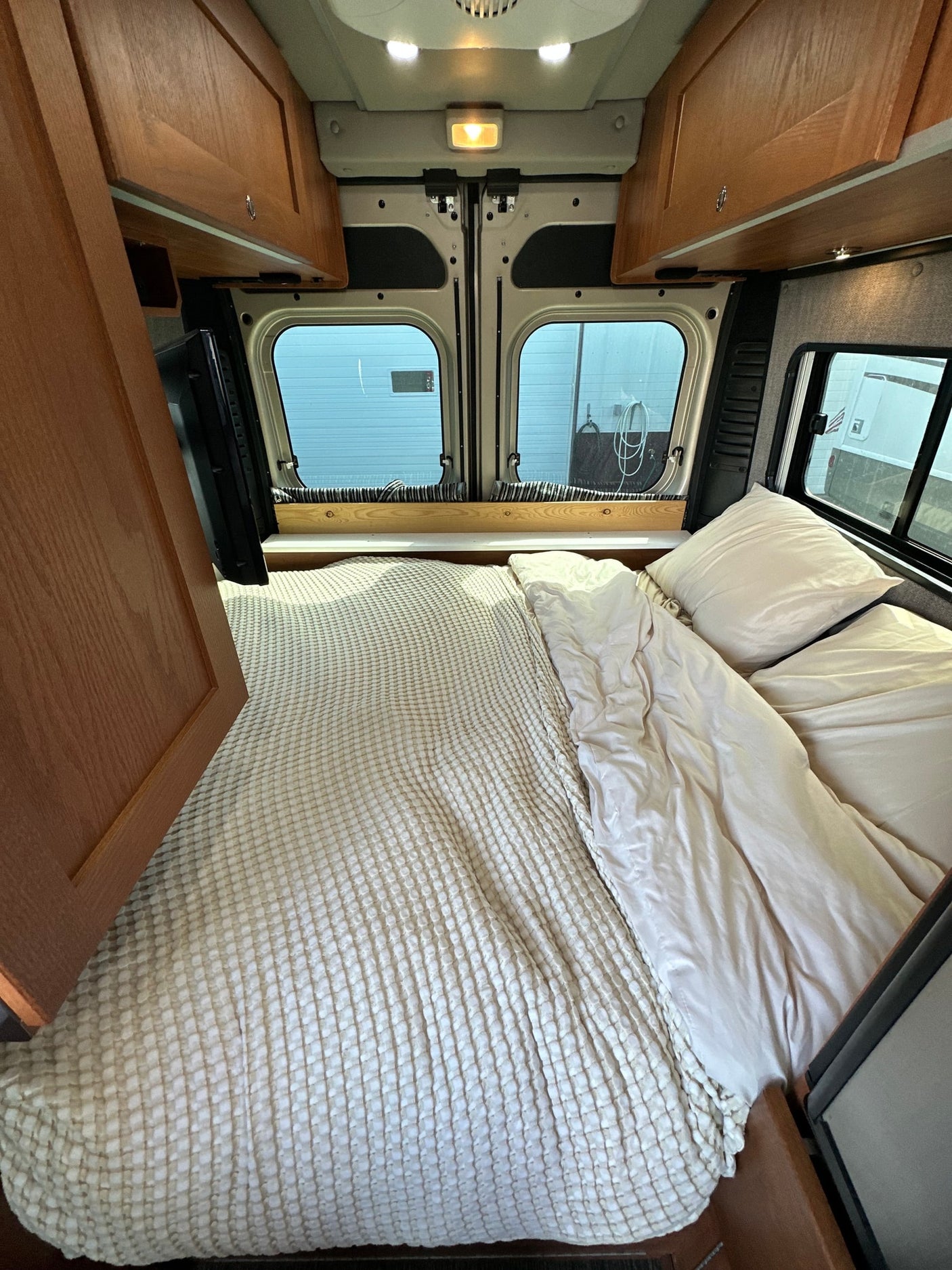 and ceiling fan. Great for mobile living.|A tan RV rental camper van and a silver travel trailer are parked on asphalt under a clear
