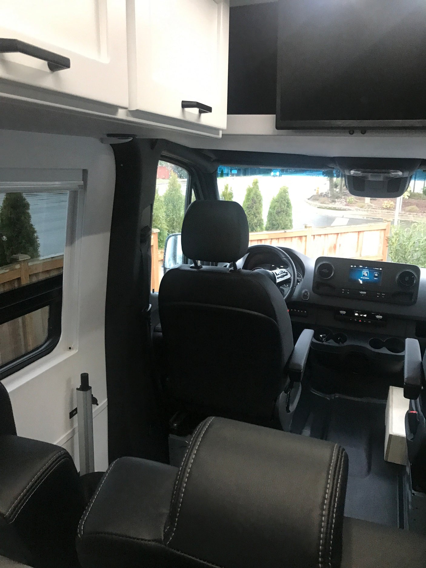 Inside this RV rental: driver's area, dashboard, passenger seating, white overhead cabinets, and an entertainment screen.