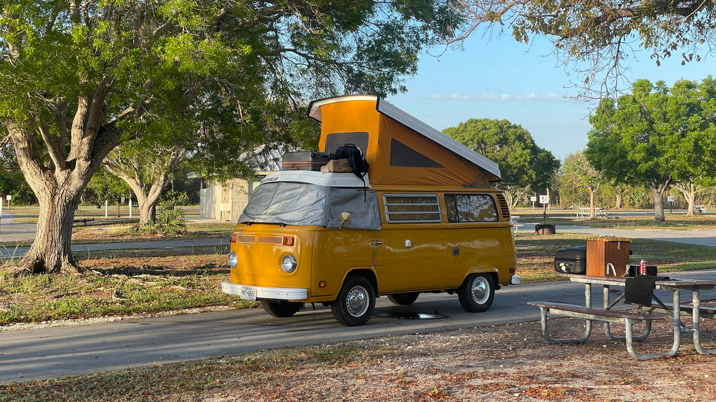 A sunny day at a campground with a vintage yellow VW camper van RV rental, pop-top raised for camping.