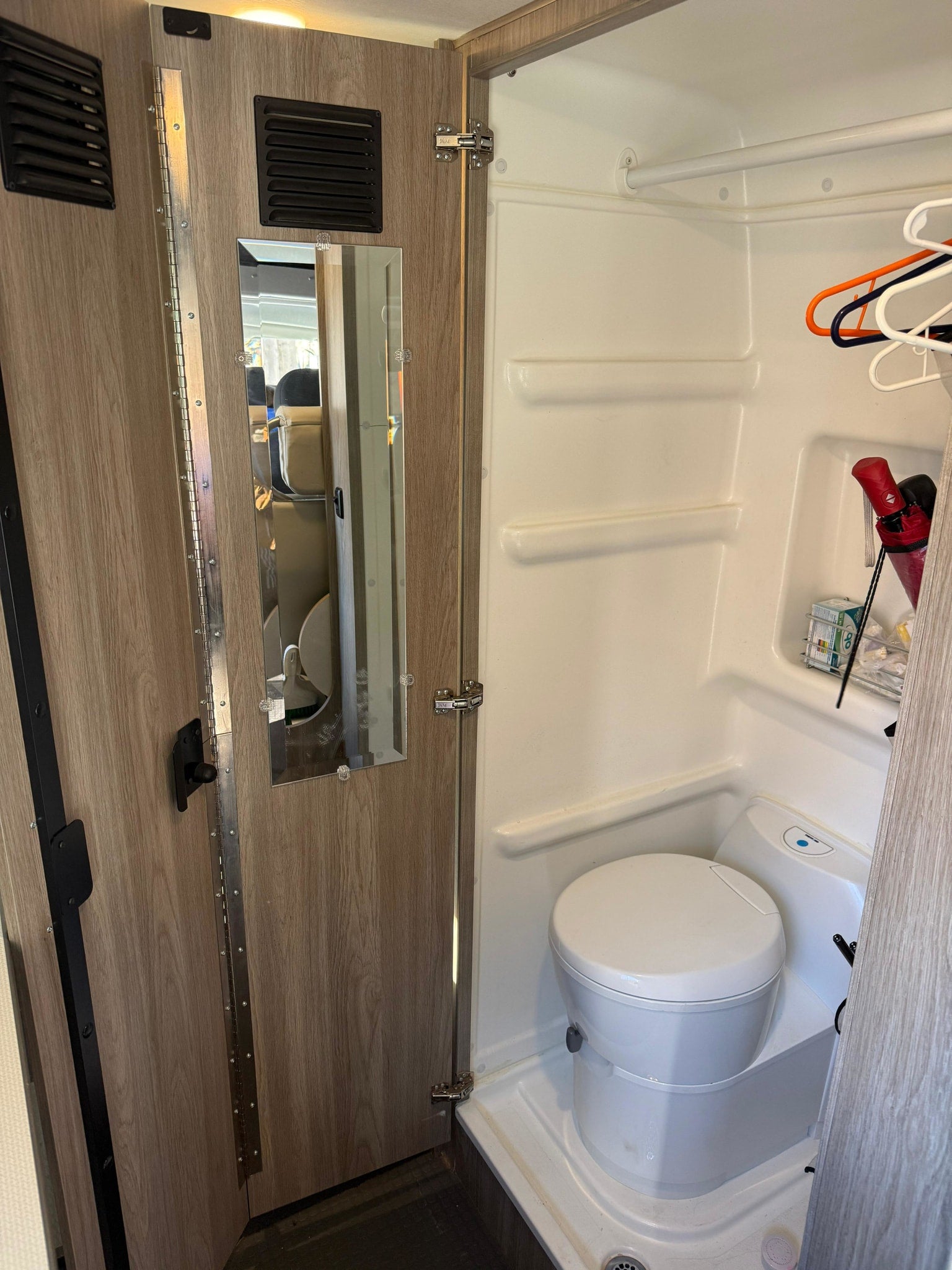 Compact RV rental wet bath with toilet, shower, and mirror door for a functional, small space.