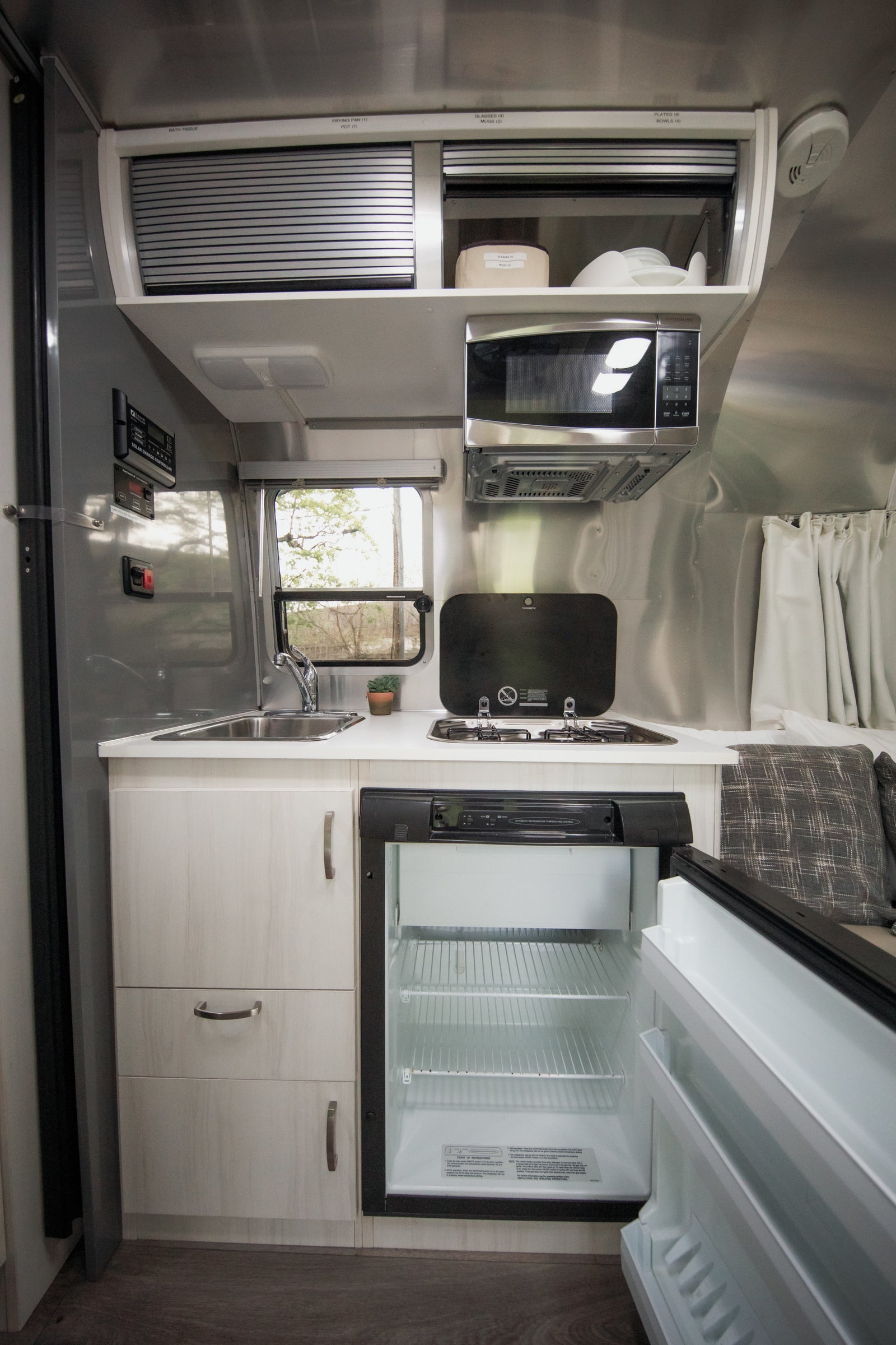 This rv rental's compact kitchen features a sink, stove, microwave, and open fridge with labeled overhead storage.
